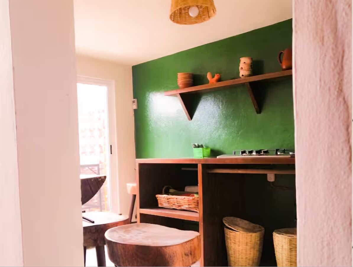 Una habitación con pared verde, estantes de madera, cestos de mimbre y una silla.