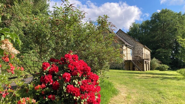 A stone building with a balcony, surrounded by lush greenery and red flowers.