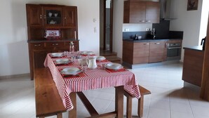 A dining area with a table set for four, wooden cabinets, a kitchen with modern appliances, and a staircase leading to another level.