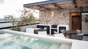 Un área de piscina en la azotea con paredes de piedra, asientos exteriores y una pérgola.