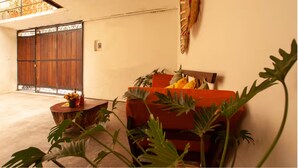 A room with a wooden door, a red sofa, a small round table with a vase, and a potted plant. - Apartment featuring Oaxacan art for two people, with parking (Oaxaca de Juárez)