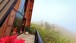 A modern building with a wooden exterior, a glass entrance, and a balcony overlooking lush greenery.