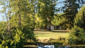A boat docked by a calm river, surrounded by lush greenery and a clear blue sky. - À l'ombre du grand pin - Bed and breakfast on the banks of the Lot and artist's studio! (Saint-Sylvestre-sur-Lot)