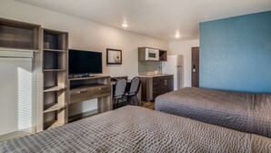Ein kompaktes Hotelzimmer mit einem Bett, einem Schreibtisch mit Stuhl, einem Fernseher, einer Mikrowelle und einer kleinen Küchenzeile.