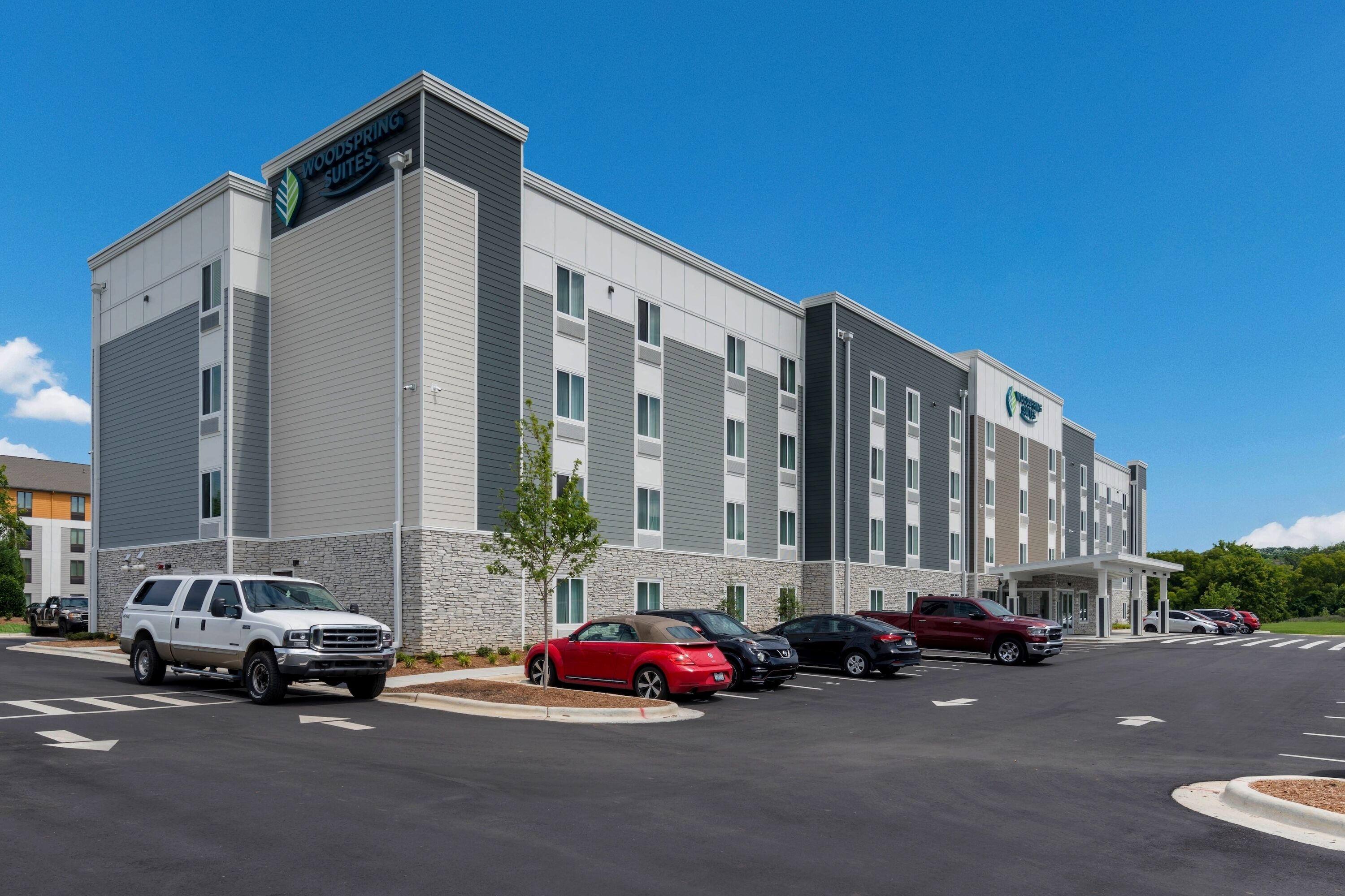 A modern hotel with a stone facade, multiple parking spaces, and a clear blue sky.