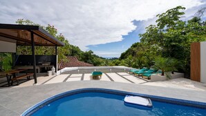Una piscina con sillas de descanso, zona de barbacoa y un área de estar techada.