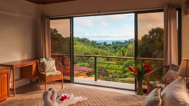Una habitación con un amplio ventanal corredera que da a un balcón con vistas de un paisaje exuberante.