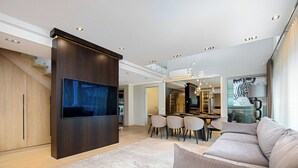 Una sala de estar moderna con un televisor de pantalla plana grande, un sofá, un comedor con sillas y una escalera que lleva a un nivel superior.