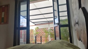 Una habitación con cama, un ventanal y vista a un espacio exterior con plantas y una cerca.