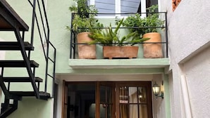 Un edificio de dos pisos con balcón, puerta de madera y plantas en macetas.