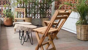 An outdoor patio with wooden furniture, including a table and chairs, surrounded by potted plants and a decorative fence. - House with Oaxacan art (Oaxaca de Juárez)