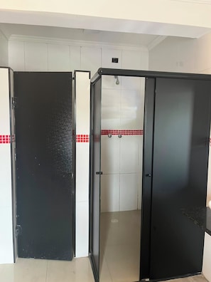 A room with a black door, a tiled shower area, and a white wall with red tiles.