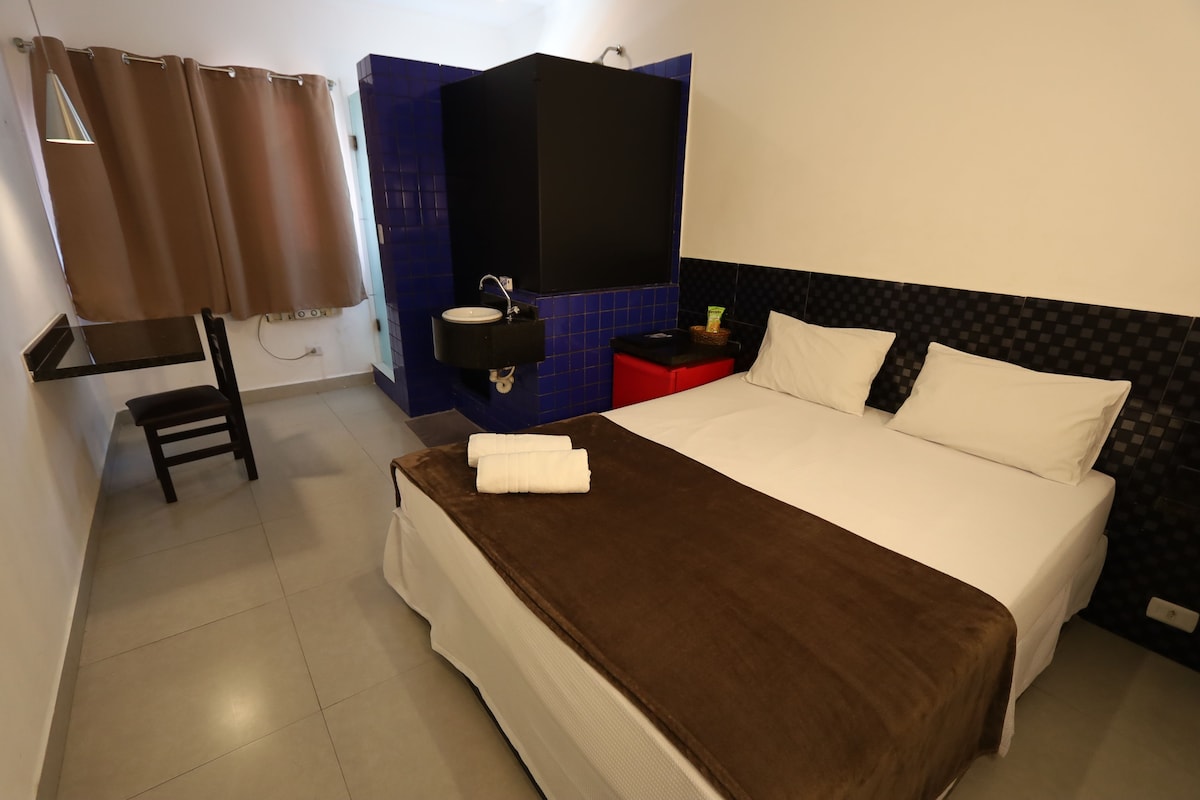 A hotel room with a bed, a bathroom, a small table, and a chair.