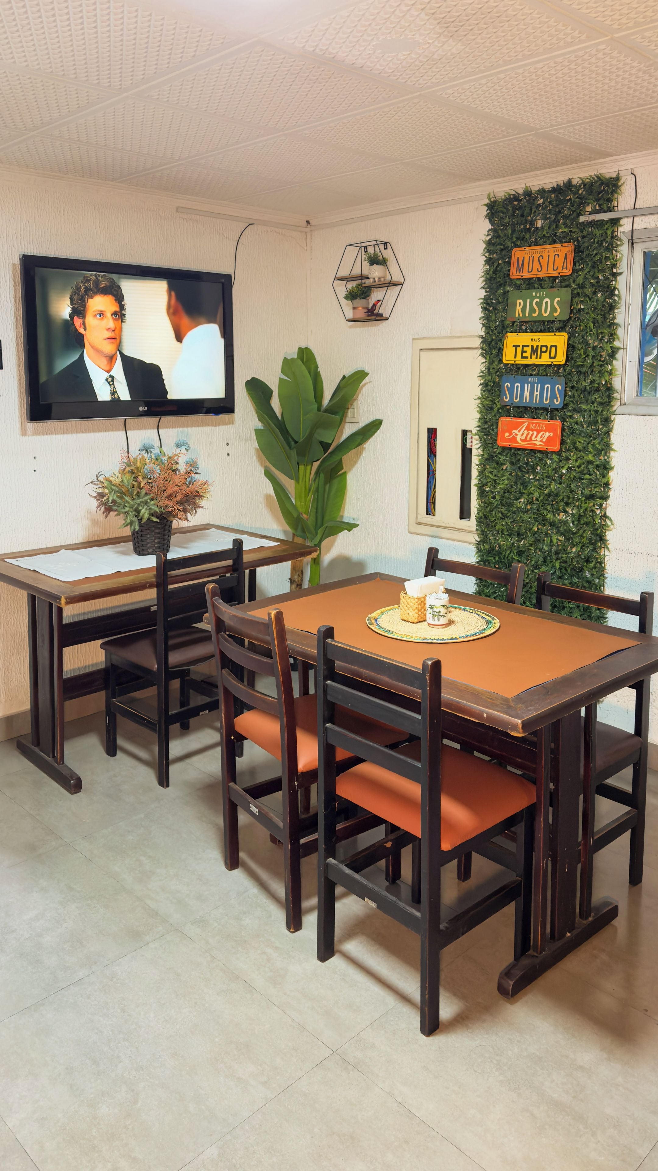 Uma área de refeições com televisão na parede, uma mesa com cadeiras e uma parede decorativa com placas.