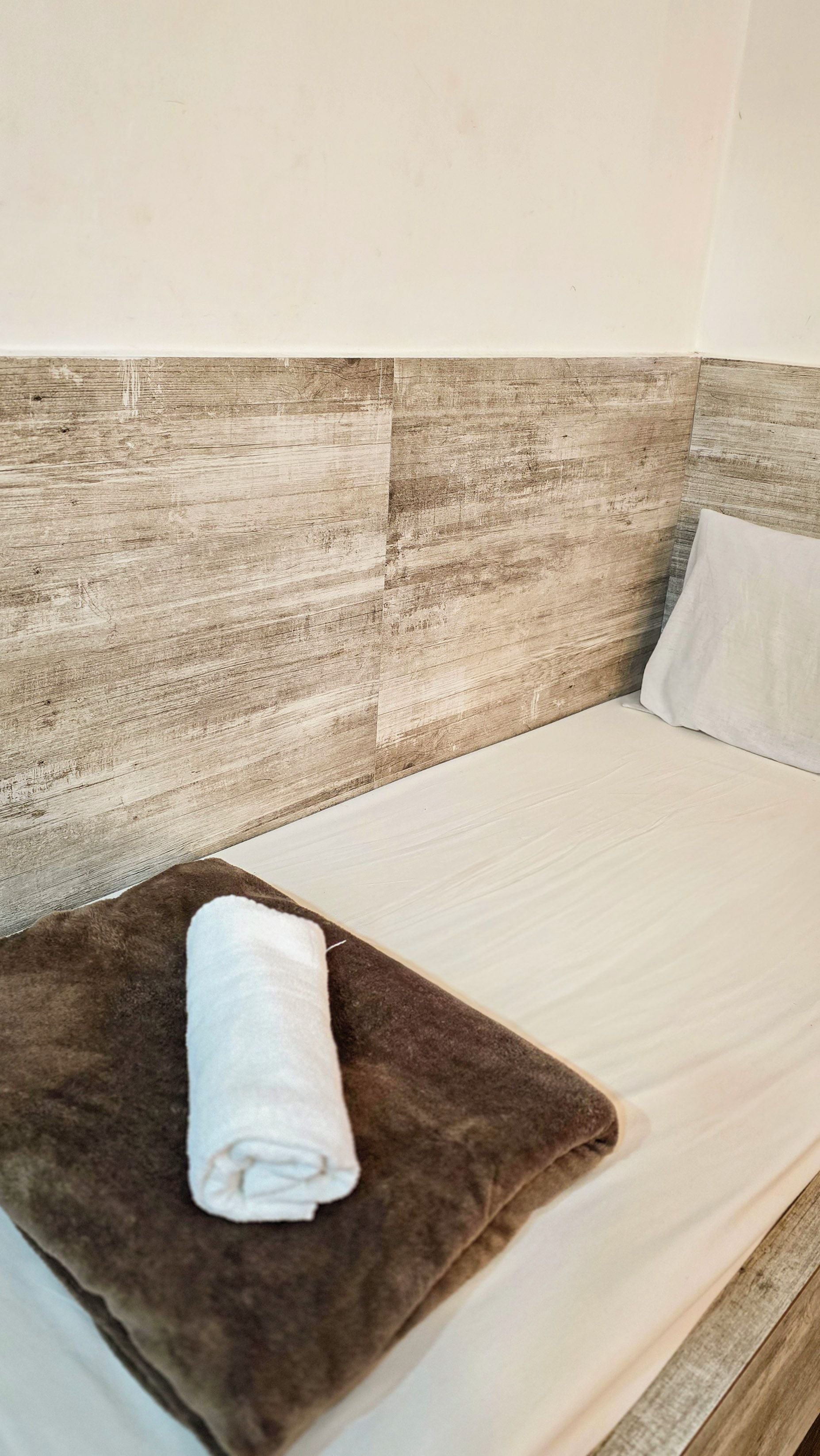 A bed with a brown headboard, a white pillow, and a rolled white towel on a brown pillow.