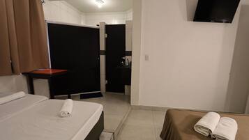 A hotel room with a bed, a table, a TV mounted on the wall, and a bathroom visible through an open door.