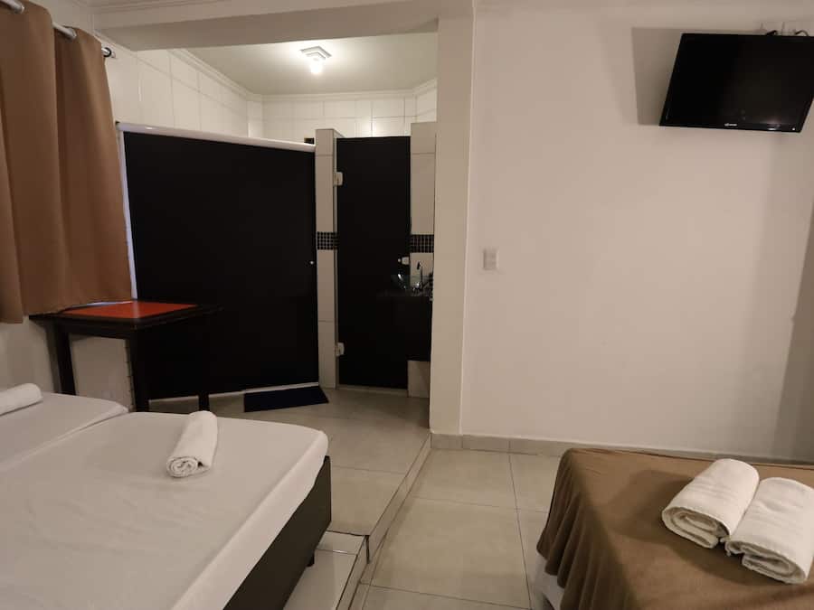 A hotel room with a bed, a table, a TV mounted on the wall, and a bathroom visible through an open door.