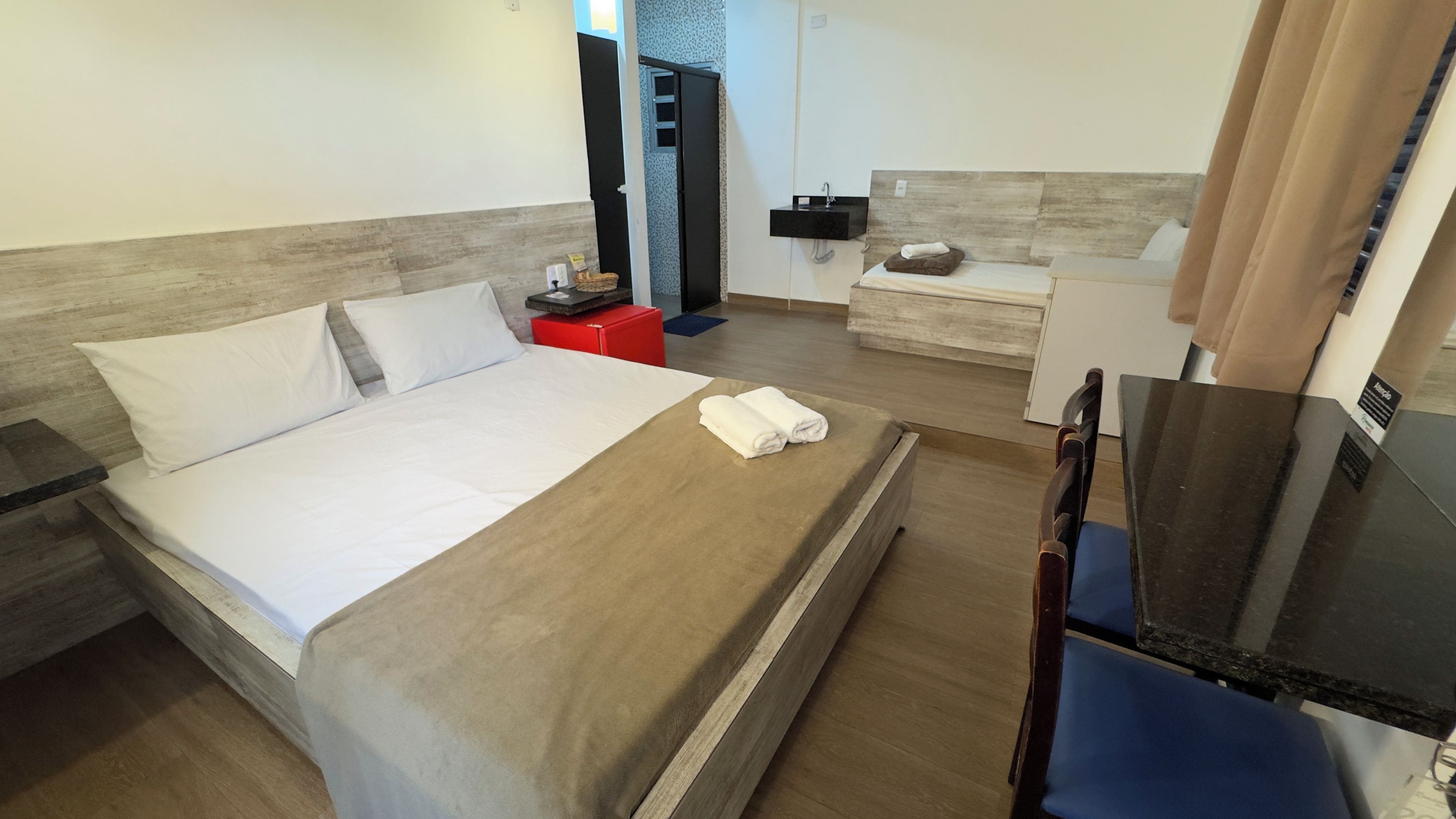 Une chambre d’hôtel comprenant un lit, un bureau, une chaise, une petite table, un lavabo et un miroir.