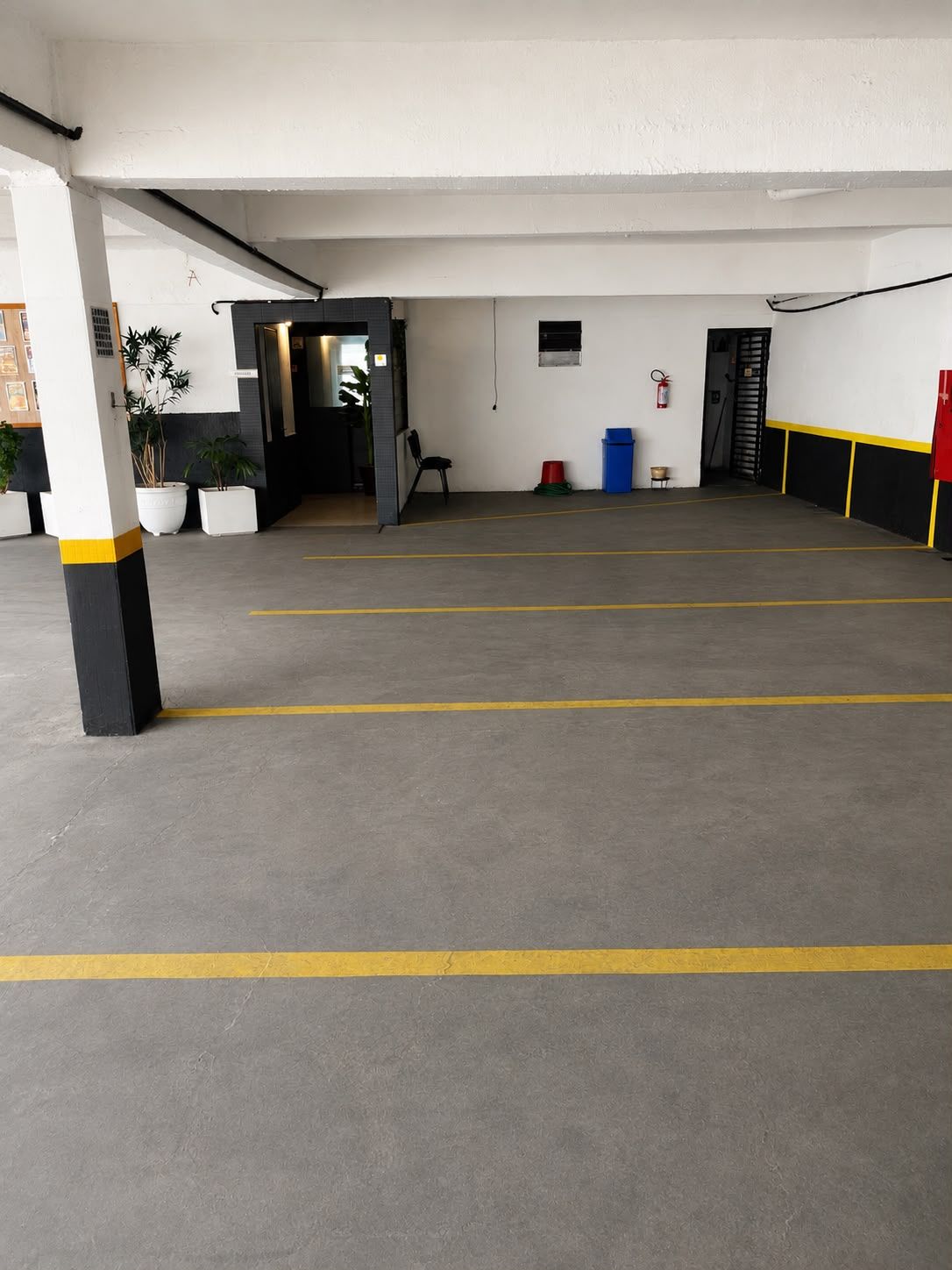 A parking garage with clear yellow lines on the floor, a fire extinguisher mounted on the wall, and a door leading to another area.
