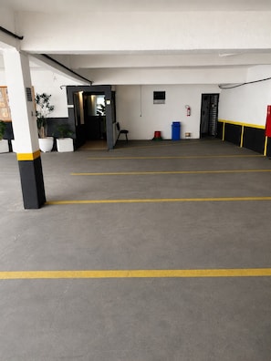 A parking garage with clear yellow lines on the floor, a fire extinguisher mounted on the wall, and a door leading to another area. - Hotel Roma Express SP (São Paulo)