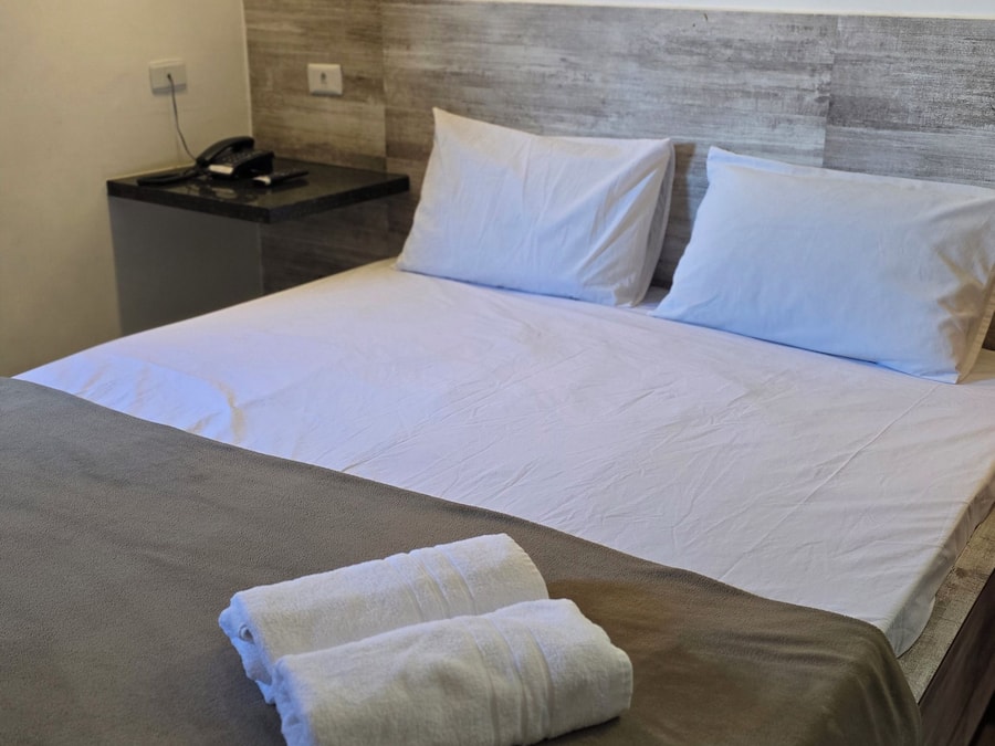 Quarto de hotel com cama, mesa de cabeceira e telefone.