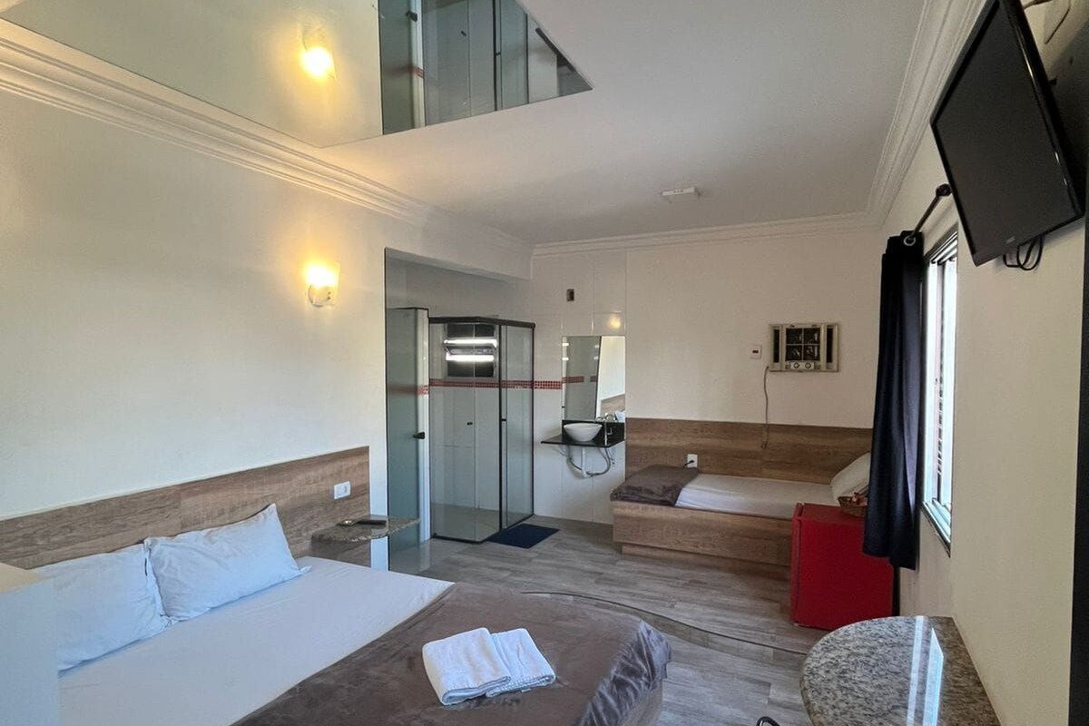 A hotel room with a bed, a desk, a TV, and a bathroom with a shower.