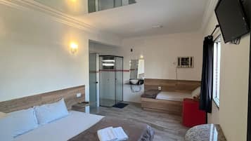 A hotel room with a bed, a desk, a TV, and a bathroom with a shower.