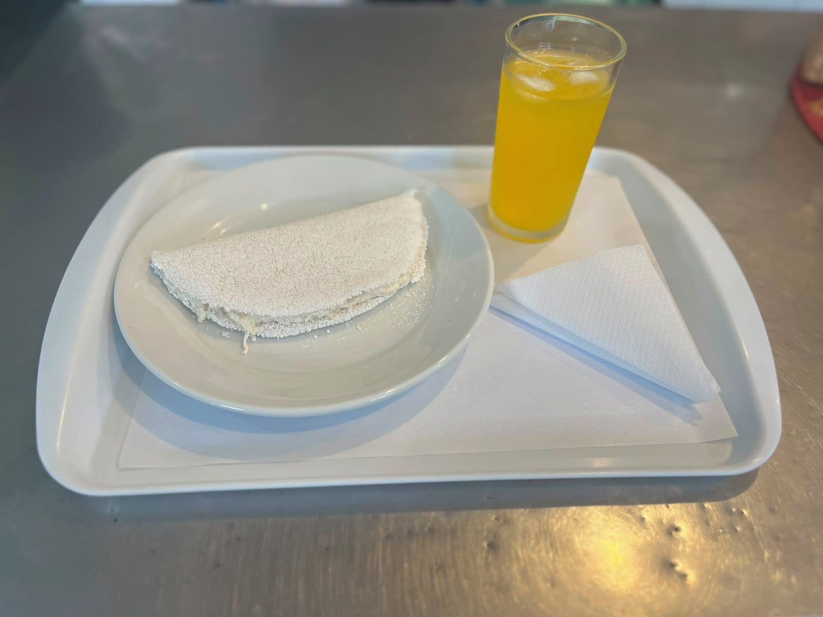 Une assiette avec une crêpe pliée et un verre de jus d’orange.