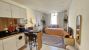 Una habitación compacta con kitchenette, cama, zona de comedor pequeña y baño.