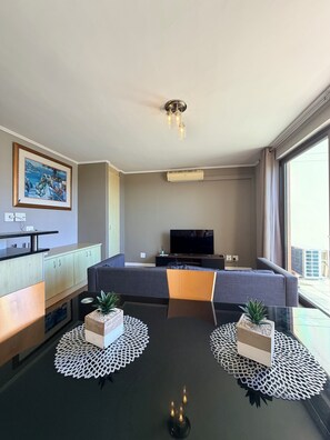 Una sala de estar moderna con un sofá, un televisor, una mesa de comedor y dos plantas en macetas.