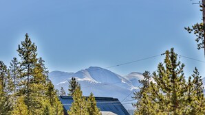 Un rifugio di montagna con tetto spiovente, circondato da alberi sempreverdi e vista chiara su montagne innevate sullo sfondo.
