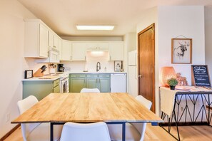 A compact kitchen with white cabinets, a wooden dining table, and a small seating area.