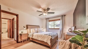 Una camera da letto con un letto, comodini, una ventola a soffitto, una finestra con tende e vista su alberi.