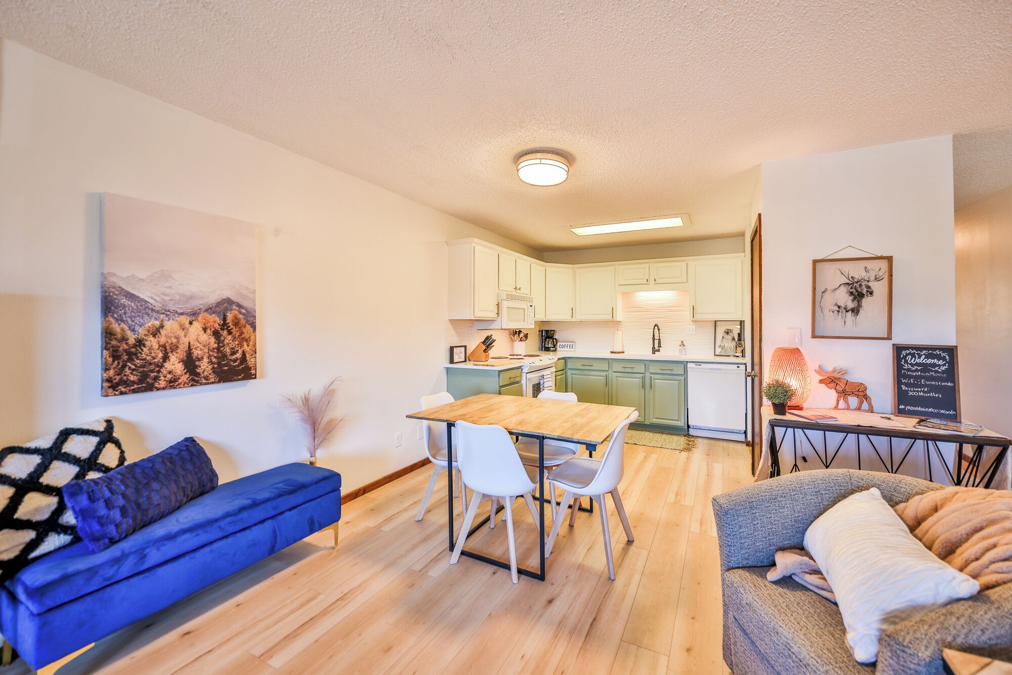 Een moderne woonkamer met een bank, een eettafel met stoelen, een keuken met kasten en een aan de wand hangend kunstwerk.