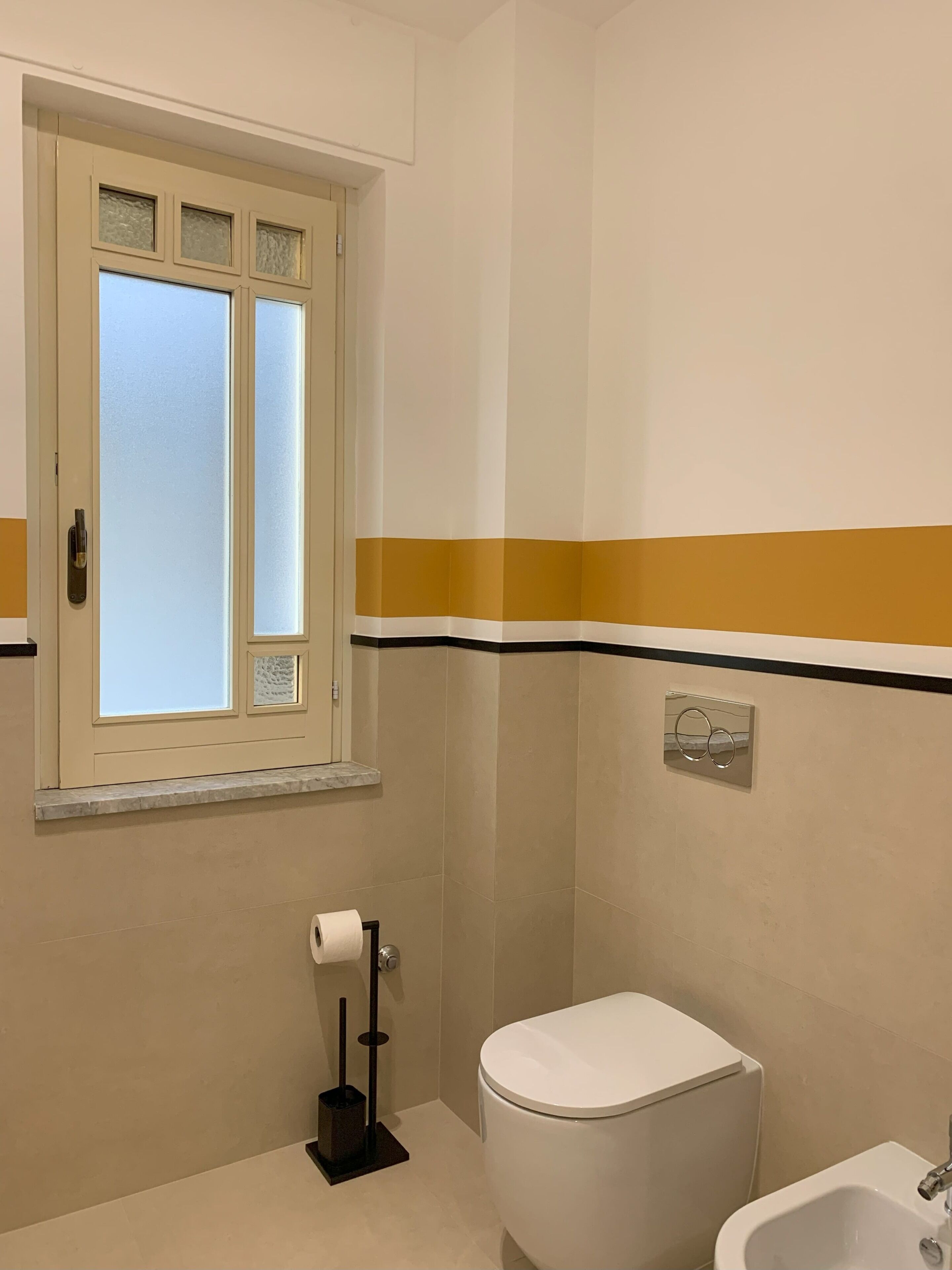 A bathroom with a toilet, bidet, and a window with frosted glass.