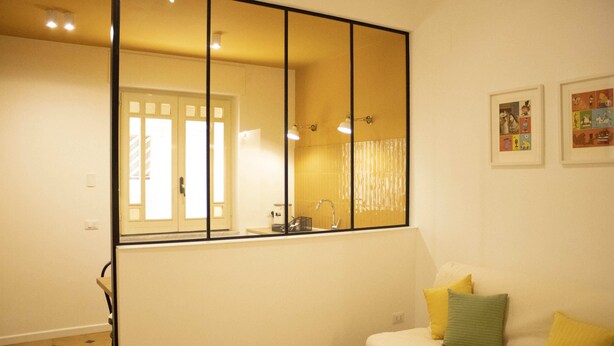 Ein Zimmer mit einem großen Spiegel, einer Couch mit Kissen, einem kleinen Tisch und einem Fenster mit Vorhängen.