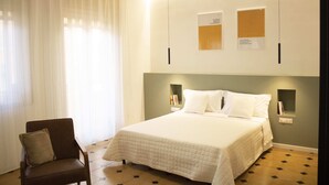 Ein Schlafzimmer mit einem Bett, einem Sessel, einem Nachttisch und Wandleuchten zum Lesen.