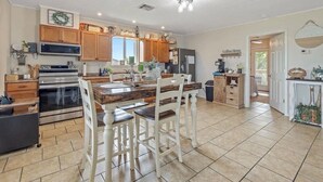 Une cuisine dotée de meubles en bois, d’un îlot central et d’un coin repas avec des chaises blanches.
