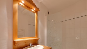 A bathroom with a wooden vanity, a white sink, a mirror with lights, and a tiled shower area. - Snowfront Stay for Four Guests (Les Deux Alpes)