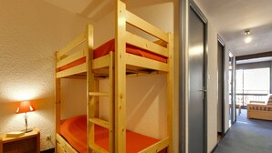 A bunk bed room with a small table and a lamp, a door to a balcony, and a view of the outside. - Snowfront Stay for Four Guests (Les Deux Alpes)