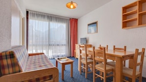 A room with a sofa, dining table, chairs, a television, and a window with curtains. - Snowfront Stay for Four Guests (Les Deux Alpes)