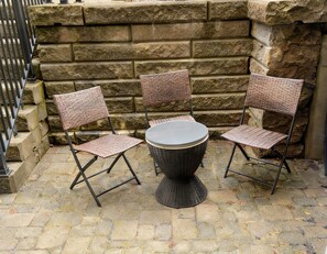 Ein Korbstuhl-Set mit Tisch, vor einer Steinmauer mit einem Metallzaun im Hintergrund.