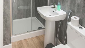 A bathroom with a glass shower enclosure, a white sink, a toilet, and a roll of toilet paper. - Central Bristol Apartment with Parking | Sleeps 6 (Bristol City)