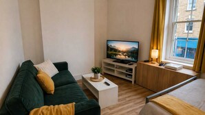 A modern hotel room with a green sofa, a bed, a TV on a wooden stand, and a window with curtains. - Central Bristol Apartment with Parking | Sleeps 6 (Bristol City)