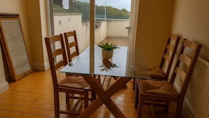 Uma sala de jantar com mesa de vidro, cadeiras de madeira e um vaso de planta.