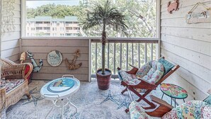 Een gezellig balkon met rieten meubilair, een klein rond tafeltje en een bloempot.
