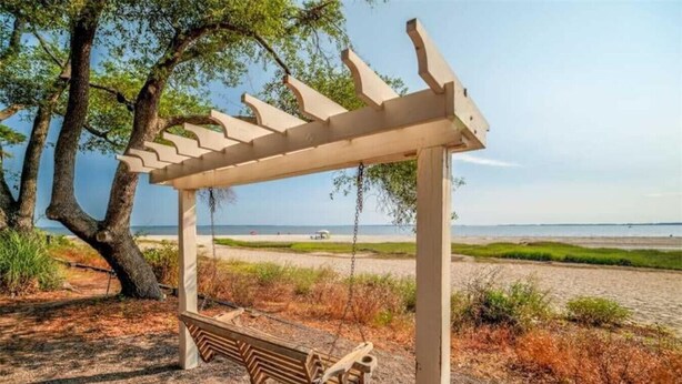 Een houten schommel met een bankje, omringd door bomen en uitzicht op het strand.
