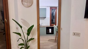 Un couloir avec une plante en pot, une porte en bois et une vue sur un coin cuisine comprenant un évier et des placards.