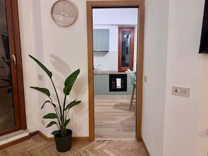 Ein Flur mit einem Blumentopf, einer Holztür und Blick in einen Küchenbereich mit Spüle und Schränken.