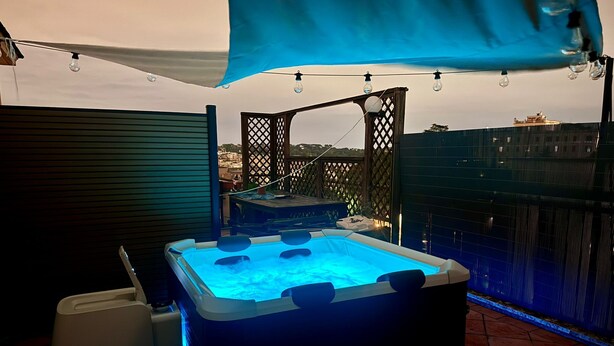 Un bain à remous avec un éclairage bleu, une terrasse en bois et une vue sur le paysage urbain.